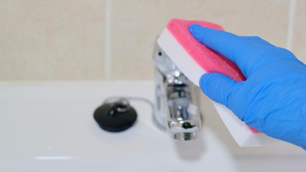 Putzfrau beim Waschen des Badezimmerhahns mit Scheuerschwamm und Handschuhen