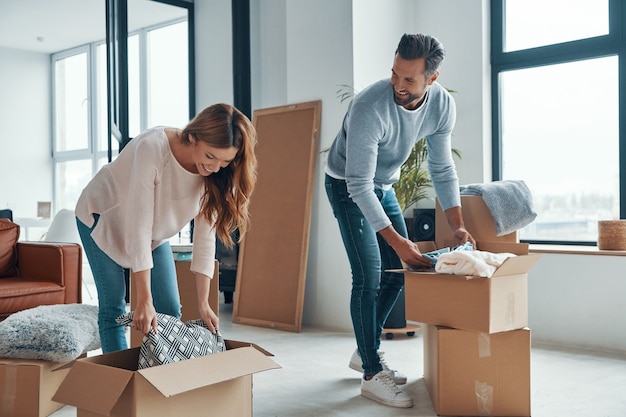 Py junges Paar lächelt und packt seine Sachen aus, während sie in eine neue Wohnung ziehen