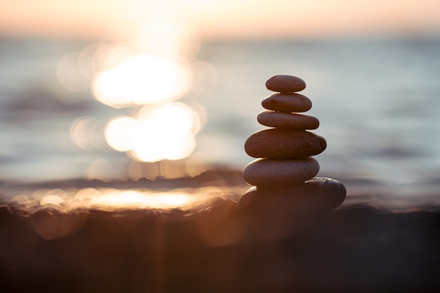 Pyramide von Steinen für die Meditation, die bei Sonnenuntergang an der Meeresküste liegt