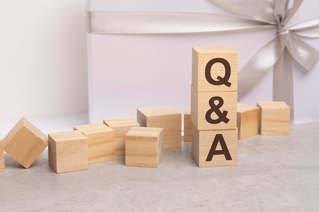 Qa-Buchstaben auf Holzwürfelkonzept auf weißem Geschenkboxhintergrund