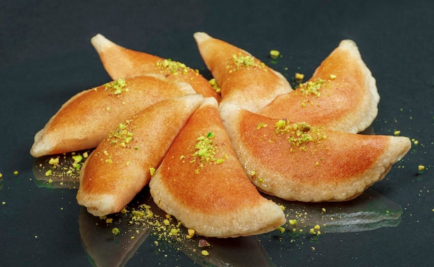 Qatayef, traditionelle arabische Ramadan-Süßigkeiten mit Pistazien auf schwarzem Hintergrund. Seitenansicht