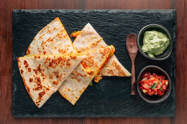 Qu Quesadillas de pollo y queso al horno servidas con salsa y guacamole en un plato de piedra.