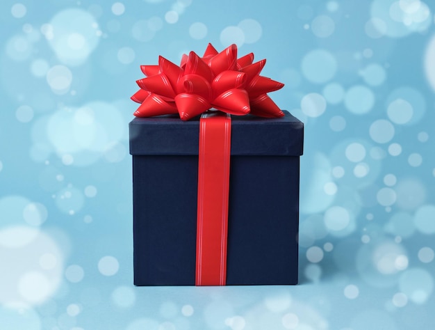 quadratische blaue Kartonbox für ein Geschenk und Seidenrote Schleife auf blauem Hintergrund
