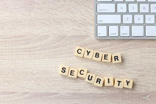 Quadratische Kacheln bilden Wort Cybersicherheit mit Computertastatur auf dem hölzernen Schreibtisch.