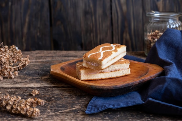 Quadratische Mini-Kuchen auf einer Holzoberfläche aus dunkelblauem Material, getrocknetem Basilikum und einem Glas Nüsse