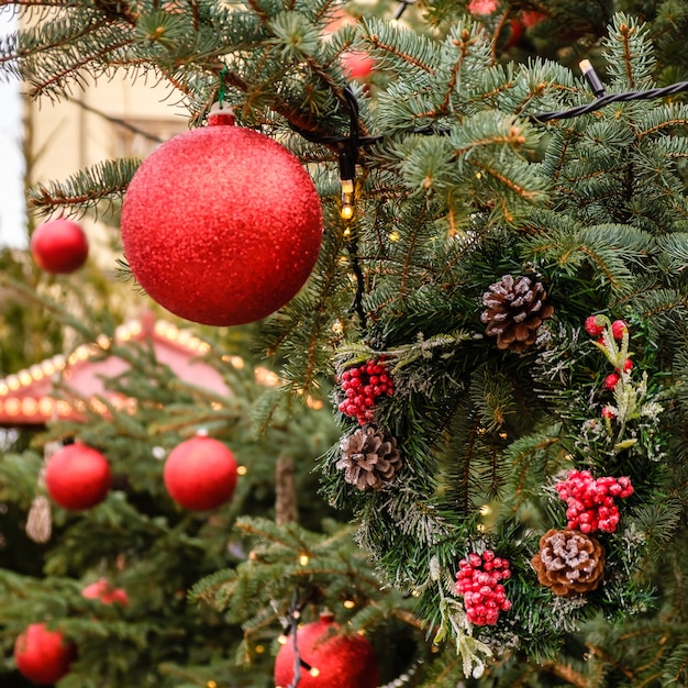 Quadratische weihnachtskarte. nahaufnahme der roten neujahrskugeln und der girlande auf den zweigen des natürlichen weihnachtsbaums draußen am sonnigen sommertag. keine leute, kein schnee.