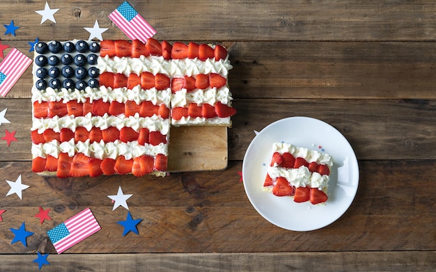 Quadratischer Kuchen mit den Farben der US-Flagge auf einem hölzernen Hintergrund mit Dekoration Teller mit Stück Kuchen Feier zum Unabhängigkeitstag