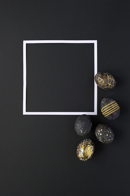 Quadratischer Rahmen mit schwarzen Ostereiern mit Goldmuster auf schwarzem Hintergrund. Luxus Ostern