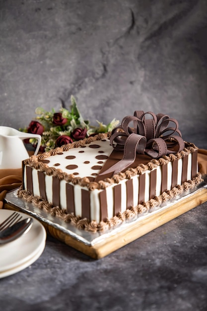 Quadratischer Schokoladenkuchen mit Rosenblüten, Löffel und Gabel, serviert an Bord, isoliert auf einer Serviette, Seitenansicht des im Café gebackenen Essens