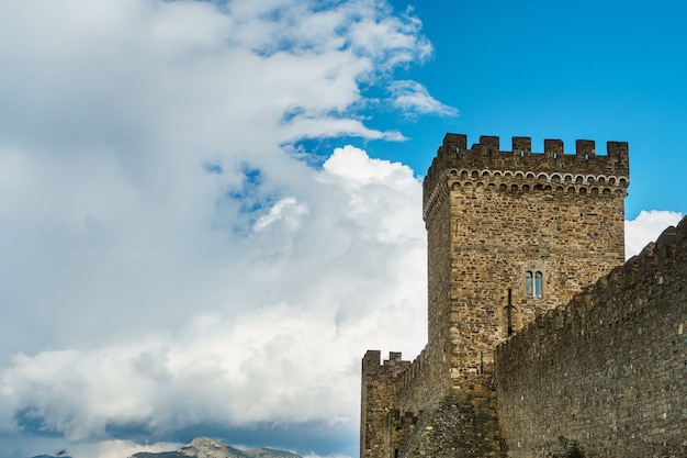 quadratischer Turm einer alten Festung mit blauem Himmel und Wolken.