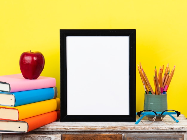 Quadro branco na mesa de madeira com pilhas de livros e fundo pastel