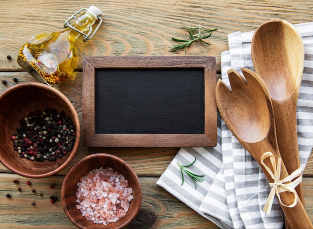 Foto quadro de giz vazio e utensílios de cozinha com especiarias em um fundo de madeira velho