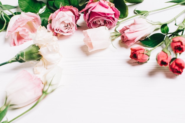 Quadro feminino de espaço de trabalho com rosas e pétalas em fundo de madeira branca. Flat lay, top view. Fundo de flores. Dia das mulheres, dia das mães.