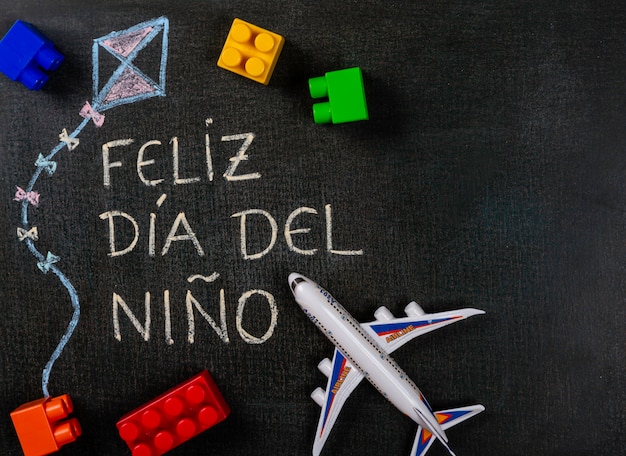 Quadro-negro escrito feliz dia del niño (espanhol). papagaio de desenho com peças de montagem e avião de brinquedo