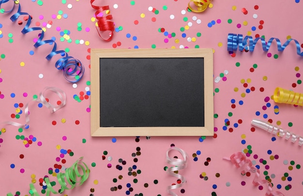 Foto quadro-negro vazio com serpentina colorida e confetes em um fundo rosa fundo de aniversário de férias