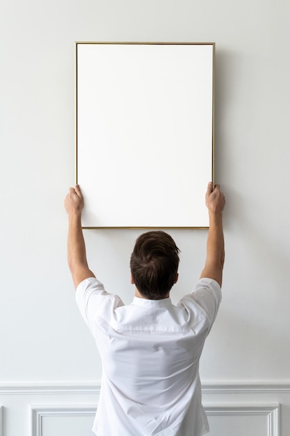 Quadro png transparente sendo pendurado por um jovem em uma parede mínima branca