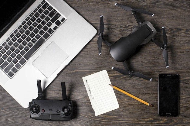 Quadrocopter em um fundo de madeira, acessórios para drones, telefone e laptop perto da folha para fazer uma lista de locais para filmagens aéreas