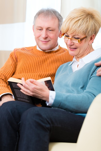 Qualidade de vida - dois idosos sentados em casa no sofá, ele abraça a esposa