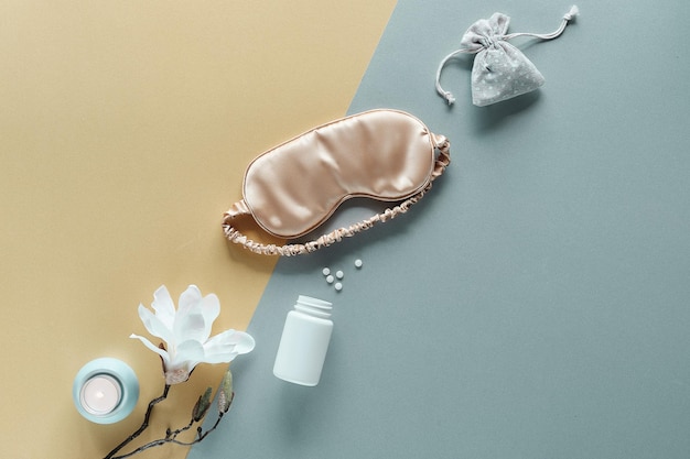 Qualidade do sono. Máscara para dormir, comprimidos para dormir, vela perfumada e saco de algodão com ervas aromáticas secas. Camada plana de papel prata ouro pálido de dois tons. Flor de magnólia branca. Fundo tonificado