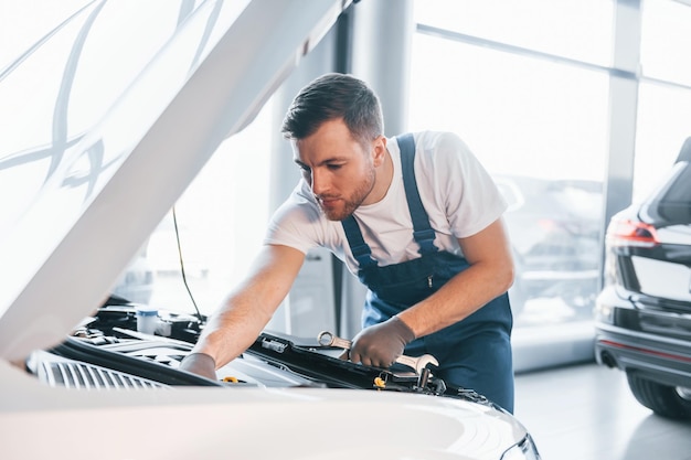 Qualitätsservice Junger Mann in weißem Hemd und blauer Uniform repariert Autos