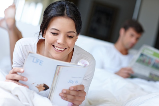 Quanto mais você lê, mais você sabe Foto de uma linda mulher deitada na cama lendo uma revista