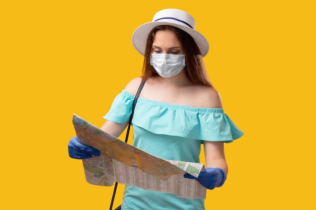 Quarantänereisen Sommerurlaub Neugierige Touristenfrau in Schutzhandschuhen mit Gesichtsmaske, die den Standort auf der Karte sucht, isoliert auf orangefarbenem Kopierraum Coronavirus-Pandemie Neue normale Urlaubsreise