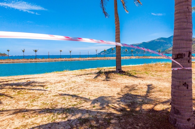 Quarentena fita vermelha e branca na bela praia exótica com céu azul claro Conceito de férias adiado viagens sem mais planos de verão e isolamento doméstico devido ao surto de pandemia de vírus corona COVID 19