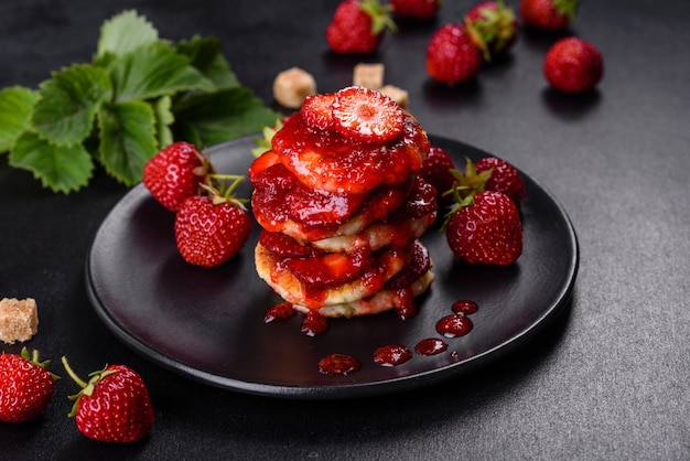 Quarkpfannkuchen mit geschnittenen Erdbeeren und Erdbeermarmelade auf einem Teller auf Betongrund