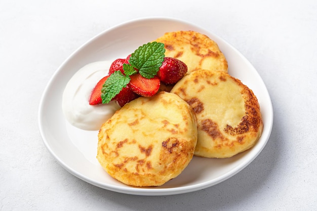 Quarkpfannkuchen mit Sauerrahm und Beeren auf hellem Hintergrund