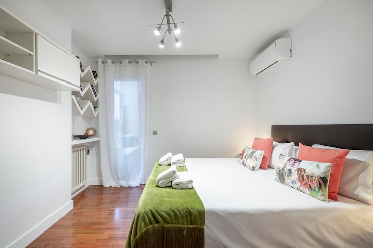 Foto quarto com cama king size prateleiras radiador de ferro fundido com almofadas mesas laterais combinando cabeceira estofada preta ar condicionado piso parquet vermelho e manta verde