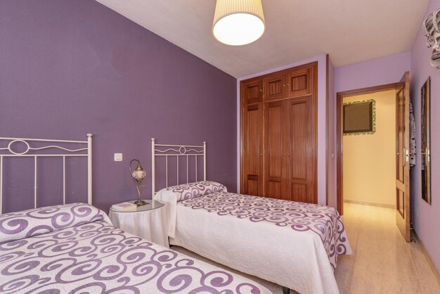 Quarto com camas individuais com colchas com padrões coloridos a condizer com as paredes e roupeiro embutido com portas em madeira