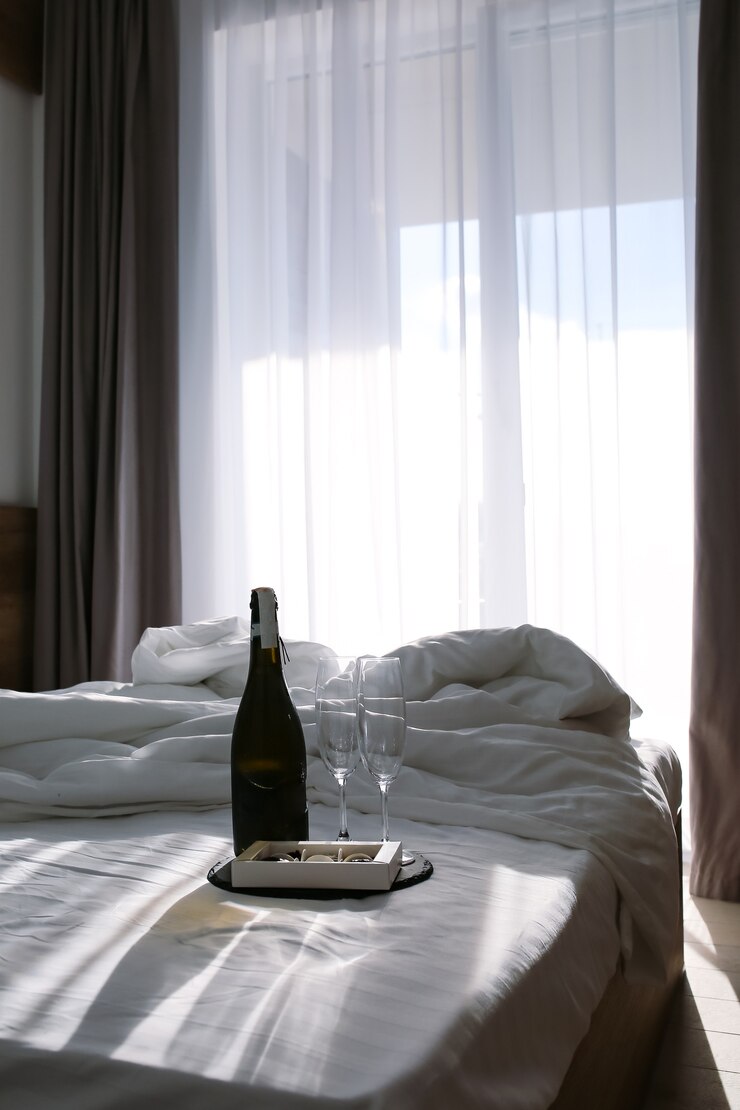 Foto quarto com uma cama propagada lençóis brancos na cama com champanhe e taças de verão o raio de sol