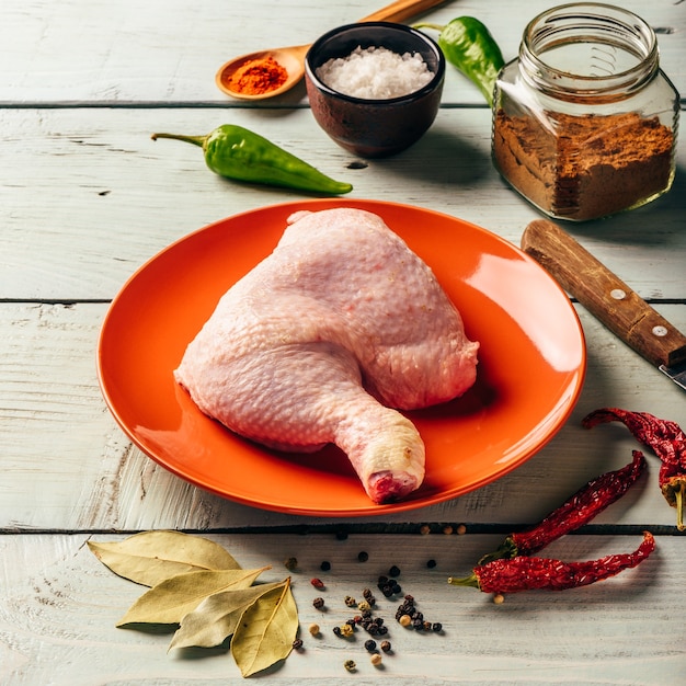 Quarto de coxa de frango no prato laranja sobre uma superfície de madeira com especiarias diferentes