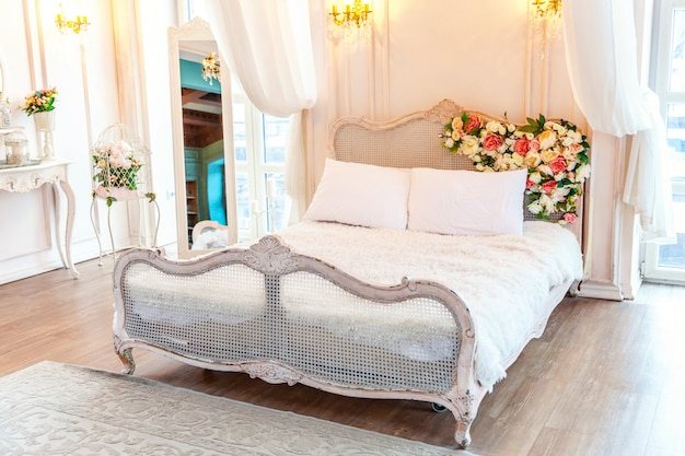 Quarto de luxo clássico branco brilhante limpo interior bonito em estilo barroco com cama king-size, janela grande, poltrona e composição de flores