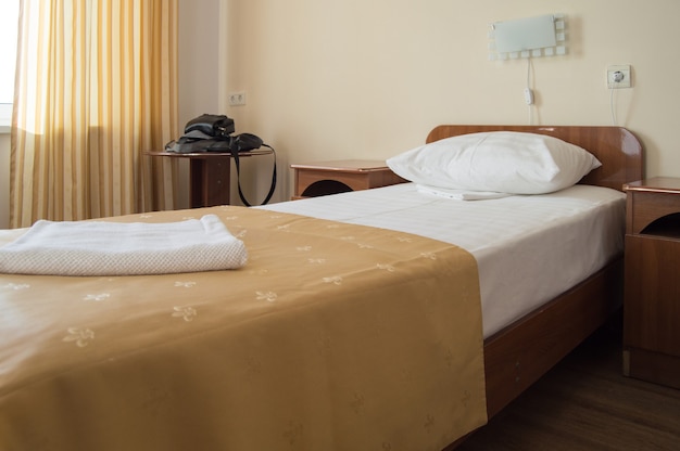 Quarto individual de hotel com cama, poltrona e mesa com malas pretas masculinas.