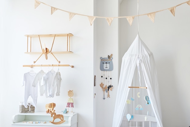 Quarto infantil com interior branco de estilo escandinavo, quarto, creche. Berço com â € ¢ dossel. Prateleiras e brinquedos em madeira. Prateleira de madeira em forma de avião