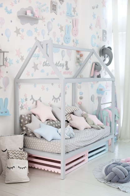 Quarto infantil vazio acolhedor com uma parede branca com adesivos, brinquedos, uma cama com almofadas. Interior escandinavo de um quarto de crianças. Cama de madeira em forma de casa com brinquedos e um cobertor. Jardim da infância