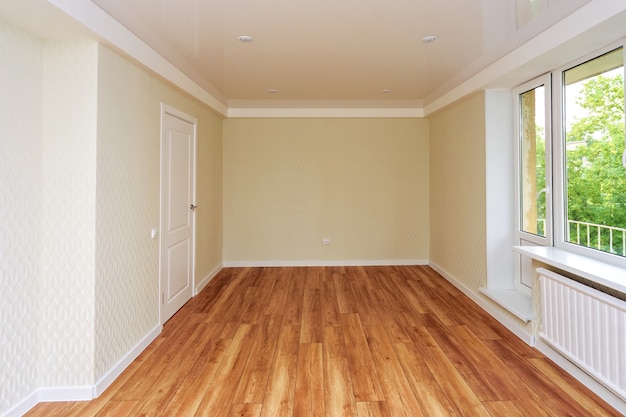 Quarto vazio e luminoso com piso de madeira e papel de parede claro. O apartamento está em reforma.