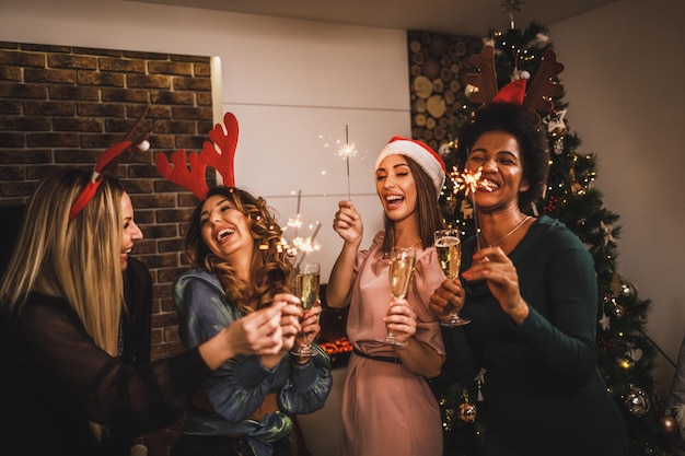 Quatro alegres garotas multiétnicas se divertindo com estrelinhas e brindando com champanhe na festa em casa de Natal ou Ano Novo.