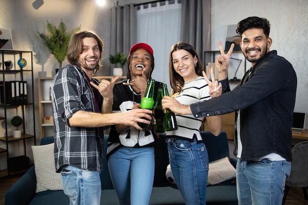 Quatro amigos multirraciais brindando com garrafas de cerveja em casa