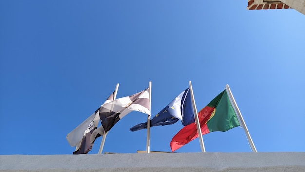 Quatro bandeiras em cima de quatro pilares do seu metal contra um céu azul portugal união europeia