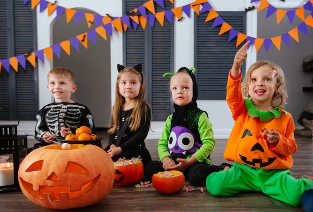 Quatro crianças em fantasias de carnaval comemoram o halloween e brincam com abóboras e doces