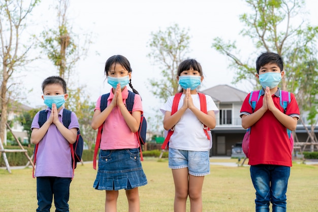 Quatro crianças pré-escolares de crianças asiáticas se encontram no parque da escola com as próprias mãos. em vez de cumprimentar com um abraço ou um aperto de mão, eles respeitam.