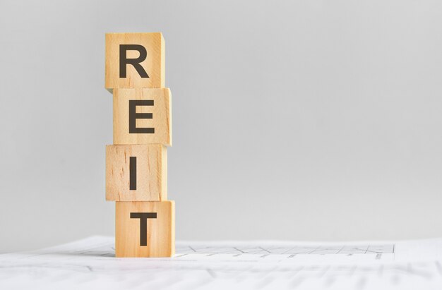 Quatro cubos de madeira com a palavra Reit no fundo de marcos financeiros brancos, forte conceito de negócio