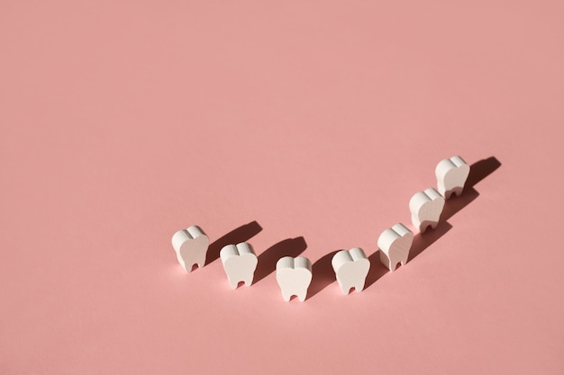 Quatro dentes falsos alinhados em um fundo rosa com um conceito de sombra profunda dental