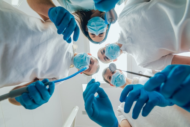 Quatro dentista de uniforme executar operação de implantação dentária em um paciente no consultório odontológico