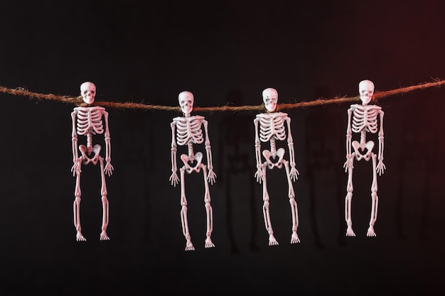 Quatro esqueletos suspensos pelo pescoço em uma corda com silhuetas em fundo escuro. Decoração de halloween
