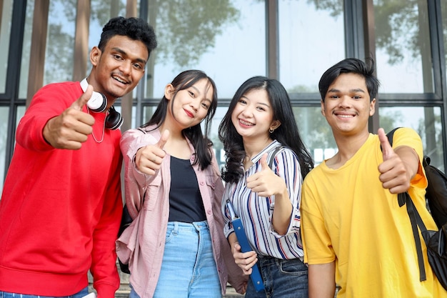 Quatro estudantes multirraciais felizes sorrindo com polegares para cima no campus universitário