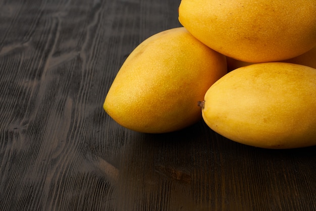 Quatro mangas de frutas inteiras na mesa de madeira. Grandes suculentas brilhantes amarelas frutas maduras em fundo escuro