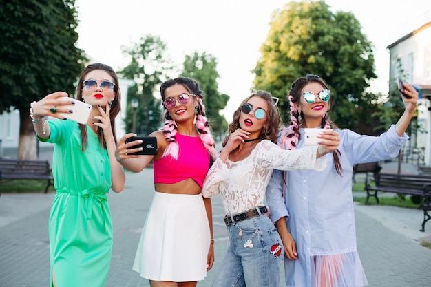 Quatro melhores amigas elegantes e lindas de óculos, cada uma posando fazendo selfies para as redes sociais, se divertem. mulheres em óculos de sol depois de fazer compras e salão de beleza.